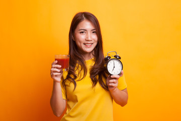 Young Asian woman with tomato juice and clock in yellow dress