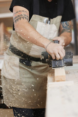 Carpenter working with electric planer on wooden plank in workshop. Hands and planer close up.