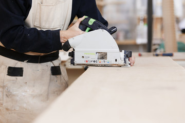 close-up of a circular saw in the hands of a man on a wooden desktop. Craftsman makes own...