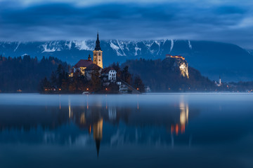 Bled lake and castle with water reflection at dawn with moody cloudy sky, Slovenia, Europe