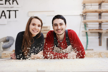 young happy family standing at a work bench in a carpentry workshop, writing a project. Family...