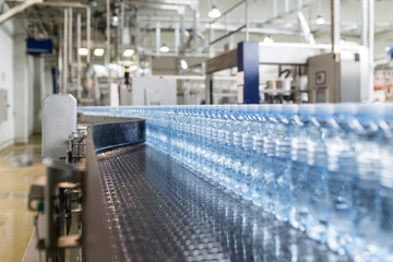 Water factory - Water bottling line for processing and bottling pure spring water into small blue bottles. Selective focus. 