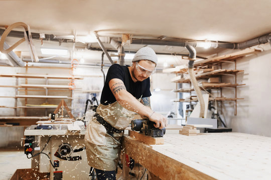 Carpenter working with electric planer on wooden plank in workshop. Craftsman makes own successful small business.