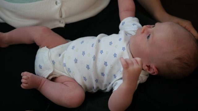 New baby on mothers lap moving his arms and legs.
