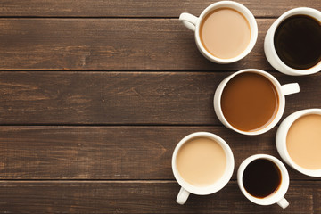 Different types of coffee in cups on wooden table, top view