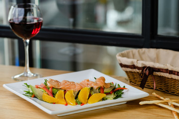 Gourmet salad with salmon and oranges on a white plate with glass of wine and bread stick