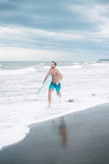 handsome smiling surfer running on beach with surfboard in Bali, Indonesia