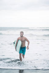 handsome smiling surfer running with surfboard in Bali, Indonesia