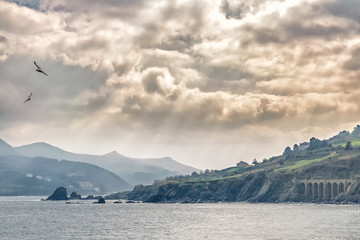 awesome sun rays between clouds with structure of stone arches and seagulls on the coast of the Atlantic Ocean in spain.