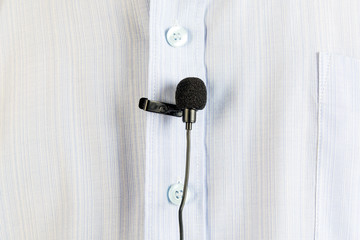 A small buttonhole microphone on a man's shirt. The man fixed the mini microphone to his blue shirt.