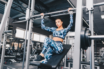 Fototapeta na wymiar Young woman with ponytail at the gym using fitness equipment. Satisfied girl relax and enjoying her training. She is relaxing hanging upon the bar. Close up. View from the right side