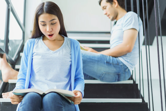 Young asian couple reading book on stairs at home. concept of knowledge examination intelligence research and education.