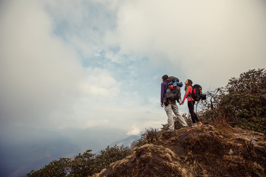 Hikers couple with backpacks relaxing on top of  mountain and enjoying view of valley above clouds