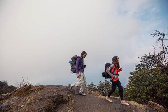 Hikers couple with backpacks walking on top of mountain and enjoying view of valley above clouds