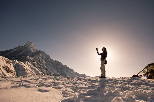 Silhouette of traveller photographer relaxing on top of snow high mountain and enjoying view of Fishtale mountain, sunrise time, strong travel concept