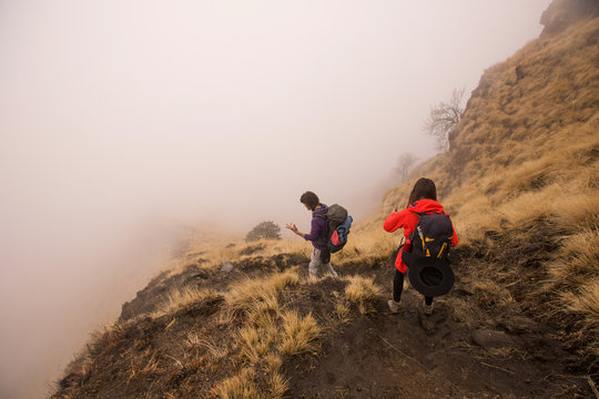 Group of people hikers walking in white fog mountains top above clouds and precipice