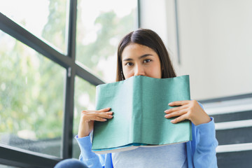 Young asian girl happy reading book on stairs at home. concept of knowledge examination intelligence research and education.