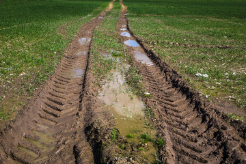 Tractor tyre tracks running through a wet and muddy agricultural grass field