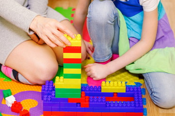 Mother with daughter built tower from toy bricks

