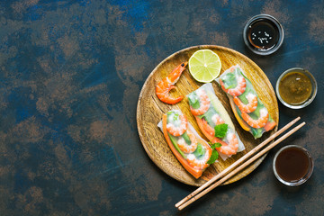 Asian food spring rolls with shrimps on a dark rustic background. Spring rolls in rice paper with a variety of sauces. Top view, space for text.