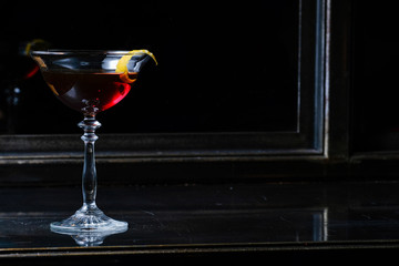 Beautiful tall glass of cocktail in front of the mirror and black background on the wooden black table.