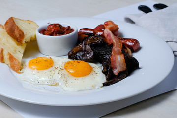 Fried eggs with bacon, sausages and bread on the white table. English breakfast
