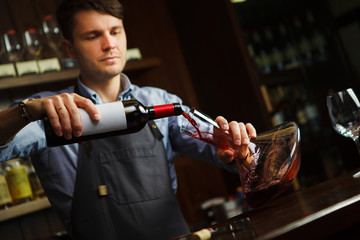 Sommelier pouring wine into glass from decanter. Male waiter