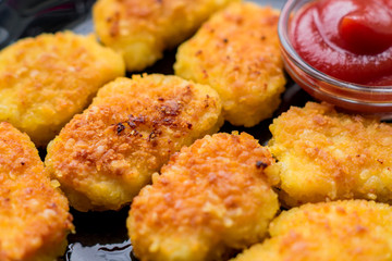 Fried crispy chicken nuggets with ketchup on black plate