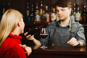 Bartender at bar counter pours red wine in glass