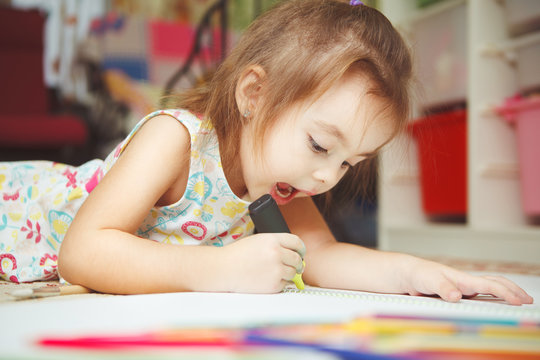 Little girl carefully draw picture in notebook with felt pen