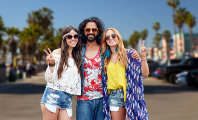 summer holidays, youth culture, gesture and people concept - smiling young hippie friends in sunglasses showing peace hand sign over venice beach in los angeles background