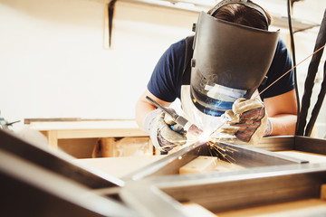 Male in face mask welds with argon-arc welding