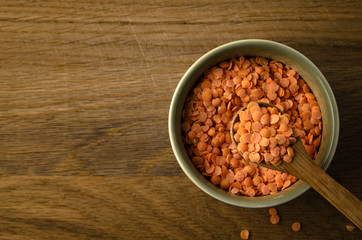 Overhead of Spoon Raising Red Lentils from Green Bowl on Oak Wood Background