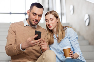 business, technology and corporate concept - smiling man and woman with smartphone drinking coffee at office stairs