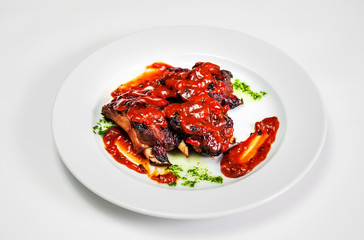 plate with fried ribs under tomato sauce with greens