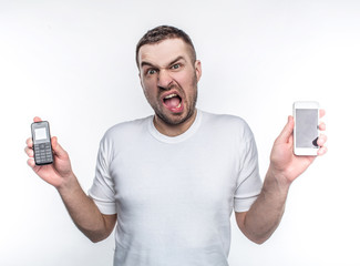 Stressed man is holding two different phones made in different years. Technologies are changing so fast that this changes are stressful to him. Isolated on white background.