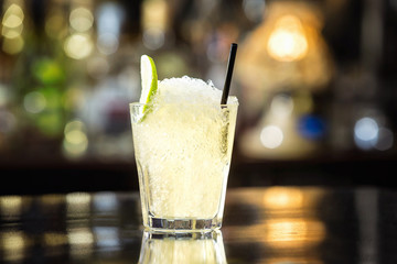 Closeup glass of soda water decorated with lime slice and frappe at bar background.