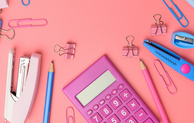 Stationary concept, Flat Lay top view Photo of Scissors, pencils, paper clips,calculator,sticky note,stapler and notepad in pink and blue tone on pink background with copy space