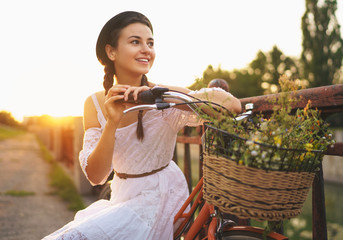 Obraz premium Young beautiful woman sitting on her bicycle with flowers at sunset