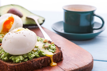 breakfast bruschetta with avocado and spinach and poached egg. with a cup of coffee