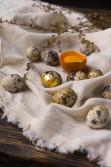 Fototapeta na wymiar Yolks of broken chicken egg in eggshell and several chicken and quail eggs decorated with dried branches on vintage style wooden table covered with crumpled sackcloth