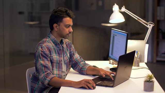 technology, deadline and people concept - programmer with laptop computer working at night office