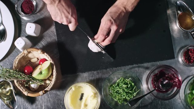Top view of unrecognizable cook cutting garlic cloves on tabletop in kitchen