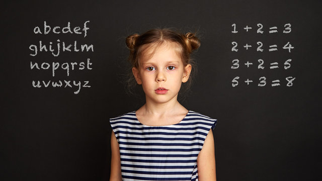 School girl standing at blackboard with alphabet and maths equations. 
