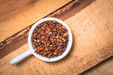 Exotic spices concept organic Chinese pepper, Sichuan pepper in white cup on wood background with copy space