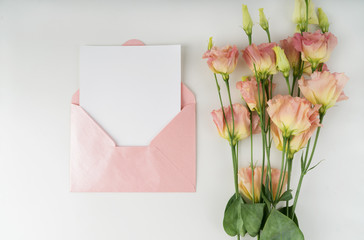 Minimal composition with a pink envelope, white blank card and flower eustoma on a white background. Mockup with envelope and blank card. Flat lay. Top view.