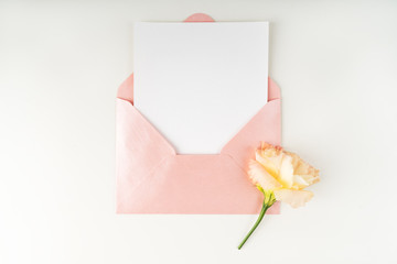 Minimal composition with a pink envelope, white blank card and flower eustoma on a white...