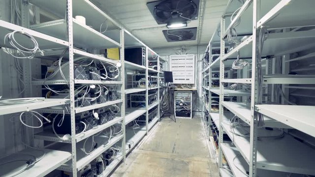 Server room for crypto currency mining. Row of bitcoin miners set up on the wired shelfs. Mining cryptocurrency. Bitcoin farm. Machines for mining cryptocurrency, bitcoin. Electronic device at day