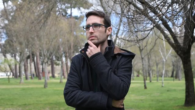 Hombre joven pensativo, cruzado de brazos y con la mano en la barbilla, en el campo