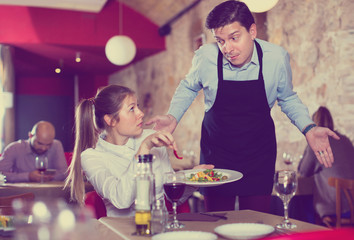 Displeased young woman conflicting with apologetic waiter because of poor quality of dish